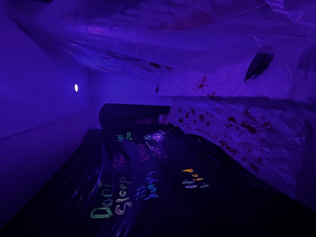 A narrow hallway under violet light, with red footprints and unsettling messages along the walls.